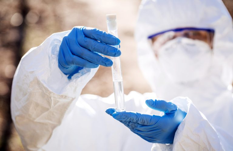 female scientist examining the liquid contents of a test tube in the forest. Ecology and environmental pollution concept.